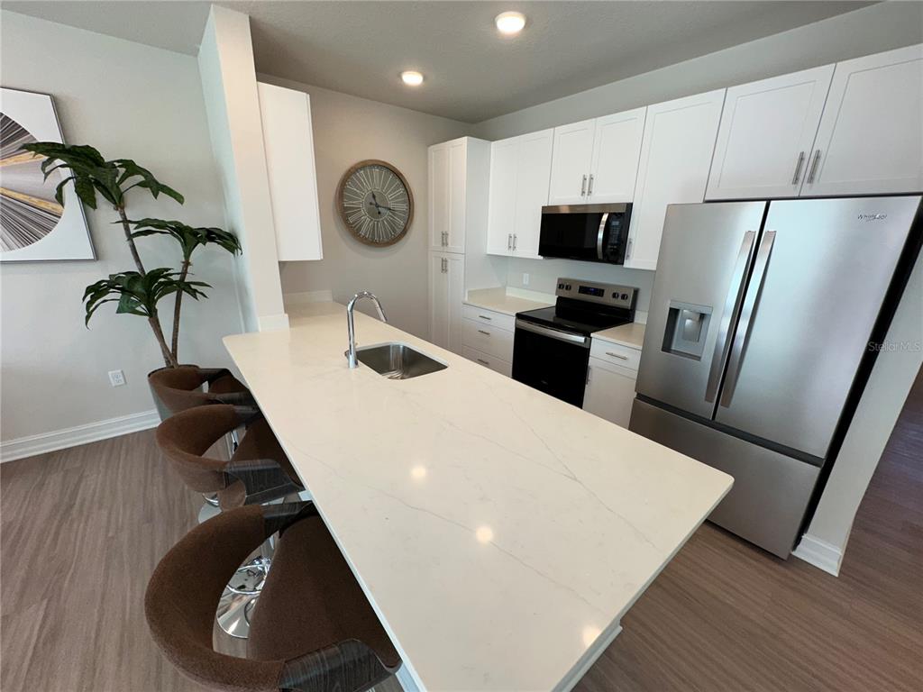 A kitchen features white cabinets, stainless steel appliances, and a large quartz-topped island with stools — 1129 E CAROLINE STREET, TAVARES, FL
