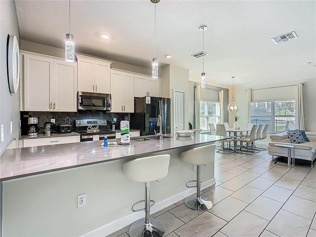 A modern kitchen features white cabinets, stainless steel appliances, and a large island with stools — 1264 CHALLENGE DRIVE UNIT 1264, DAVENPORT, FL