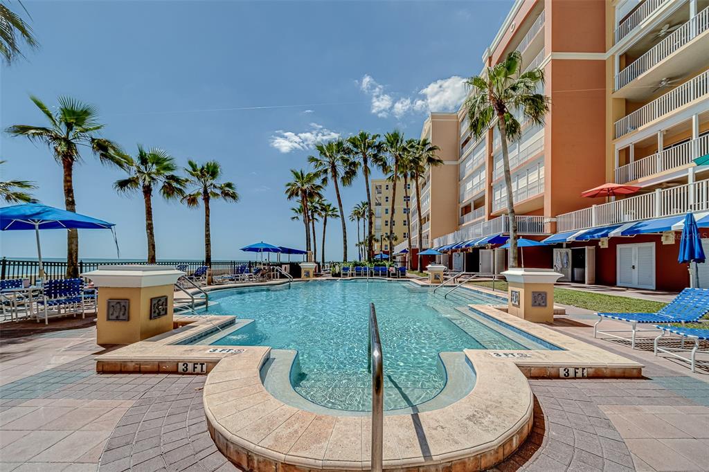A swimming pool with palm trees and a multi-story building under a clear blue sky — 16500 GULF BOULEVARD UNIT 355, NORTH REDINGTON BEACH, FL