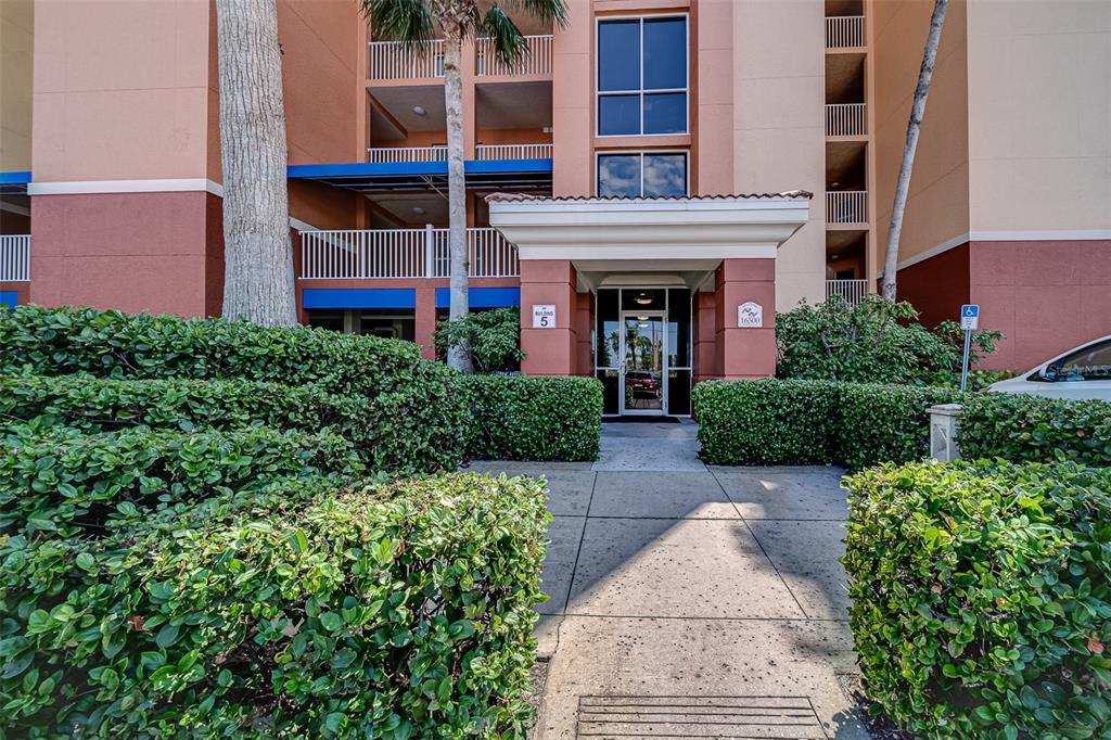 The exterior entrance of a multi-story residential building features a paved walkway and manicured hedges — 16500 GULF BOULEVARD UNIT 355, NORTH REDINGTON BEACH, FL