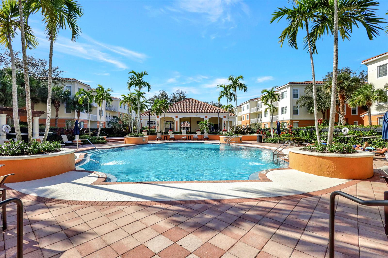 A swimming pool surrounded by palm trees and apartment buildings under a clear blue sky — 9873 Baywinds Drive # 5302, West Palm Beach FL 33411, WEST PALM BEACH, FL