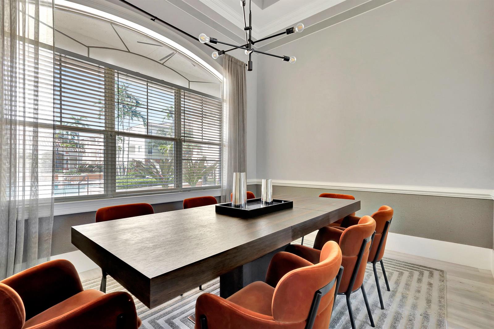 A dining room features a long wooden table, orange velvet chairs, and a large arched window — 9873 Baywinds Drive # 5302, West Palm Beach FL 33411, WEST PALM BEACH, FL