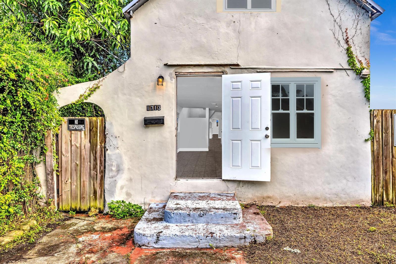The exterior of a small, weathered stucco house features an open white door and steps — 1713 NW 76th Terrace, Miami FL 33147, MIAMI, FL