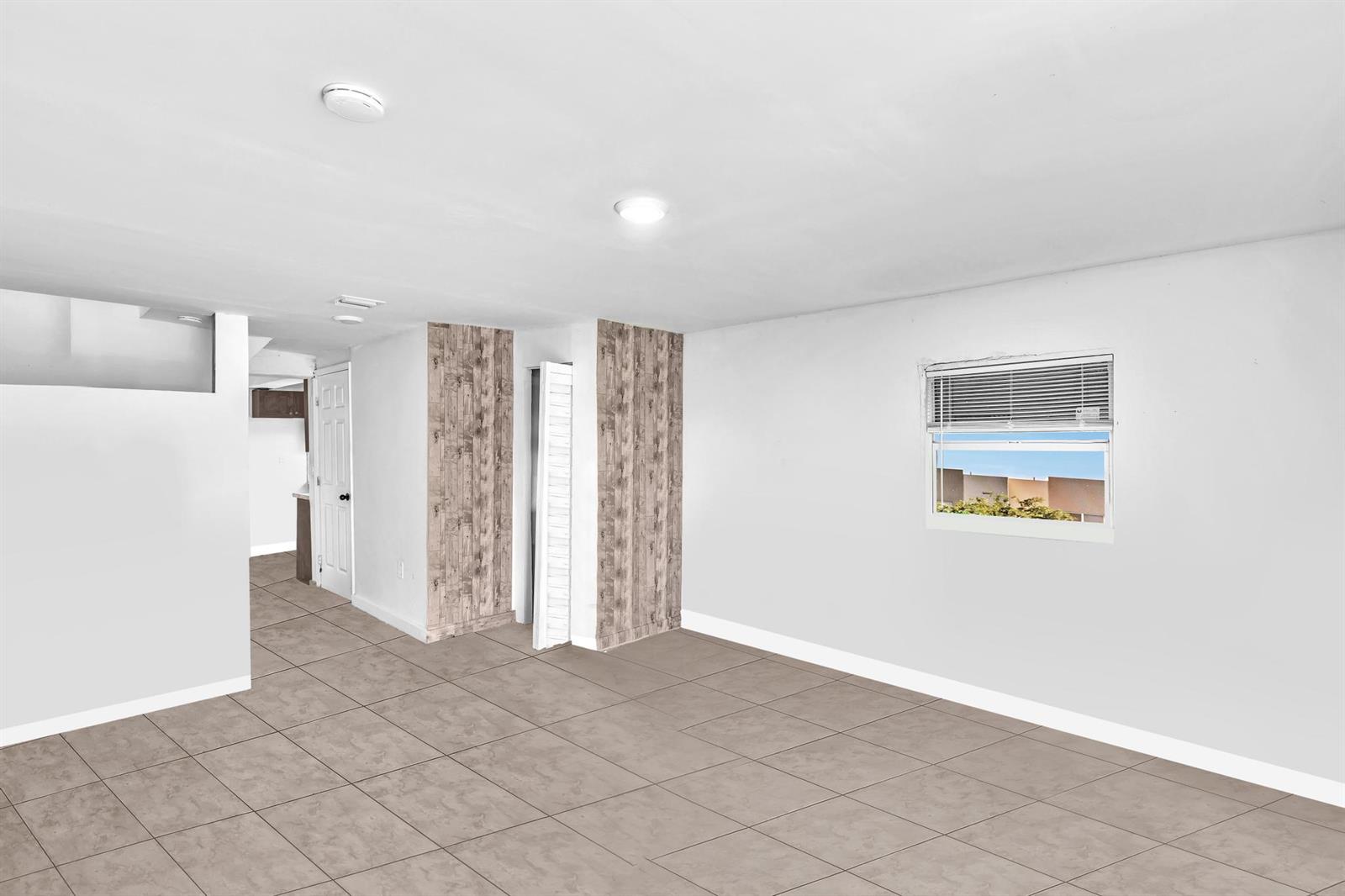 An empty room with light-colored tile flooring, white walls, and wood-paneled accent columns — 1713 NW 76th Terrace, Miami FL 33147, MIAMI, FL