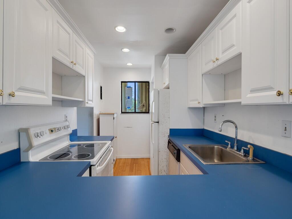 A galley kitchen features white cabinets, blue countertops, a white stove, and a stainless sink — 5373 SE Miles Grant Road # 208, Stuart FL 34997, STUART, FL