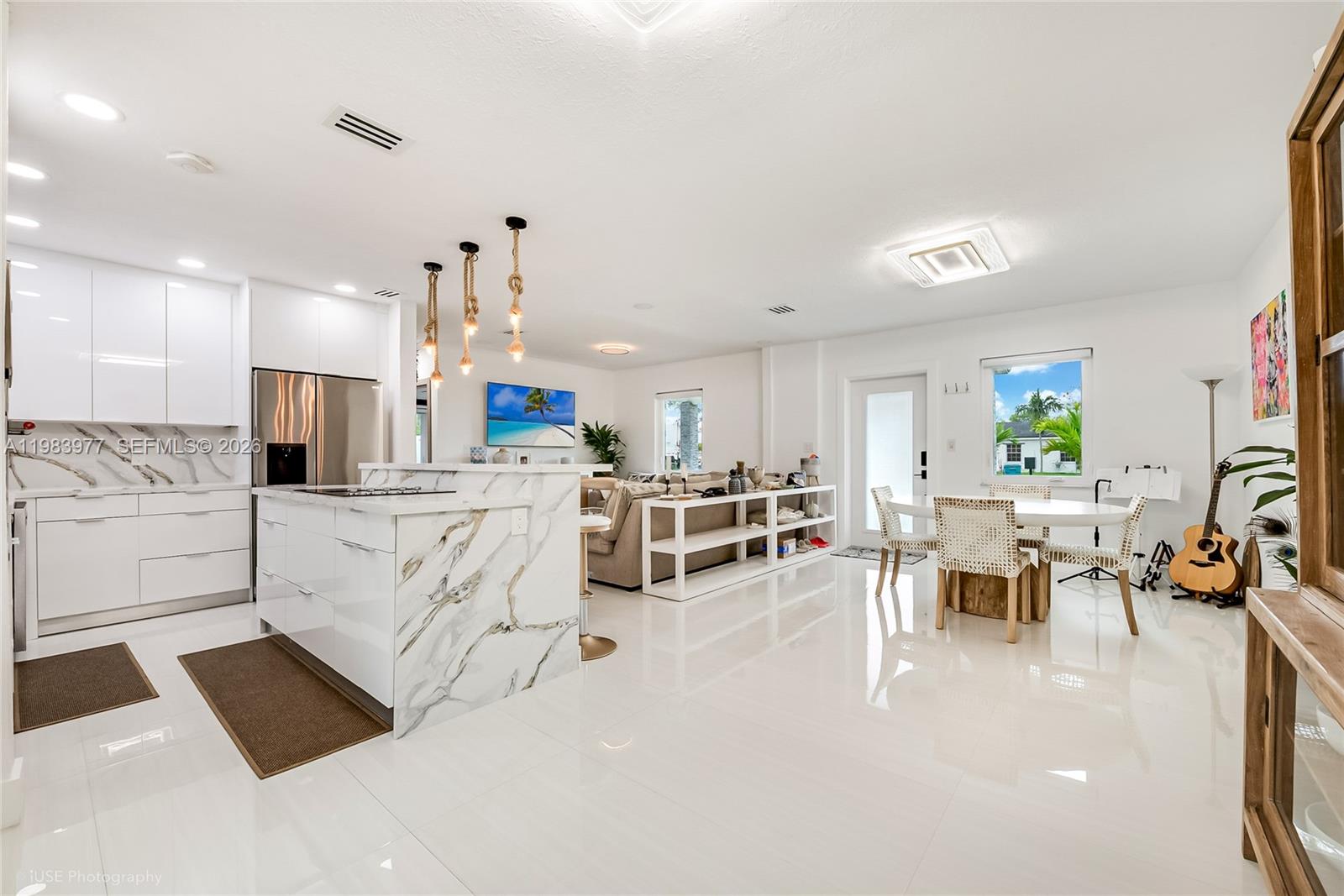 A modern open-concept kitchen and dining area features white cabinetry, marble countertops, and tile flooring — 7235 SW 39th St, Miami FL 33155, MIAMI, FL
