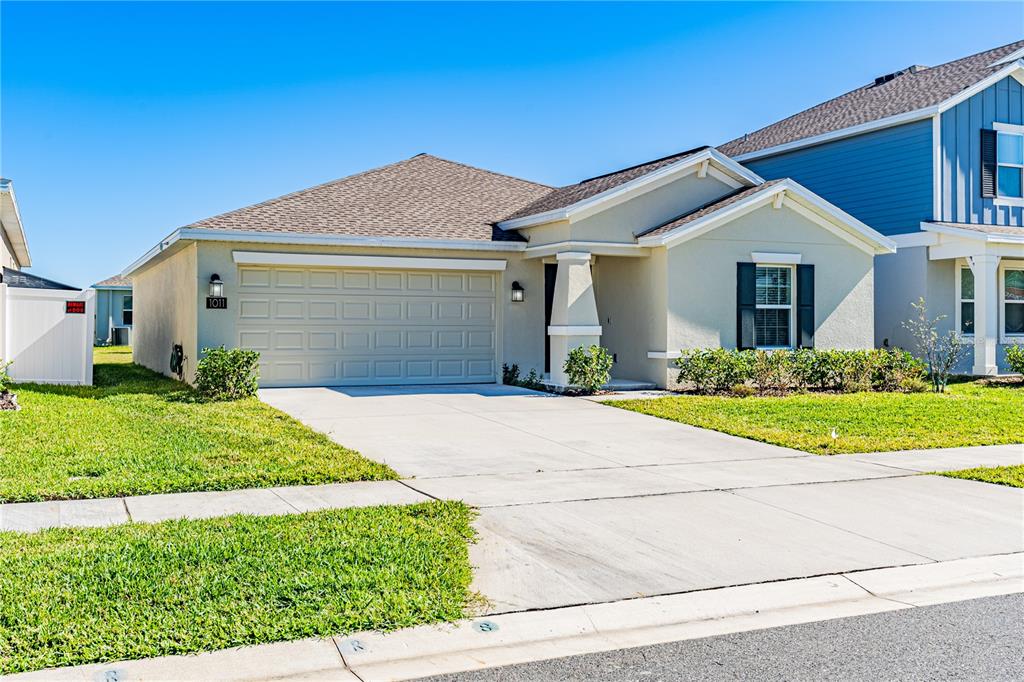 A single-story suburban house with a tan stucco exterior, a two-car garage, and a driveway — 1011 JOHN JACOB ROAD, DAVENPORT, FL