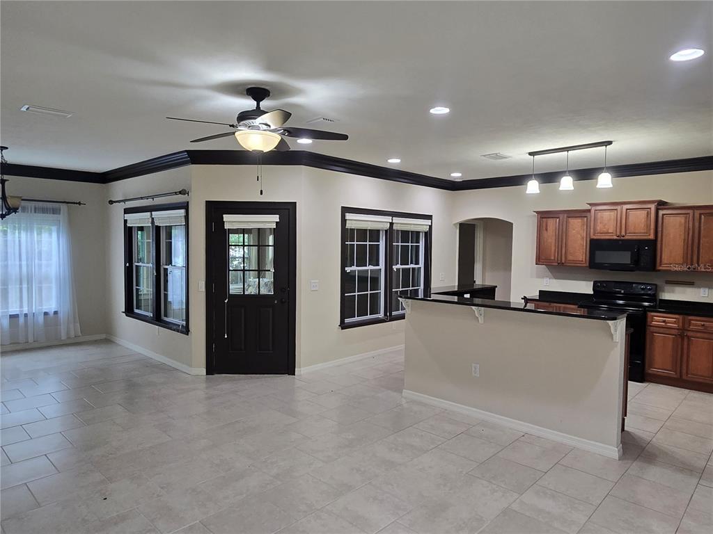 An open-concept kitchen and living area features tile flooring, dark crown molding, and wooden cabinets — 19176 NW 228TH STREET, HIGH SPRINGS, FL
