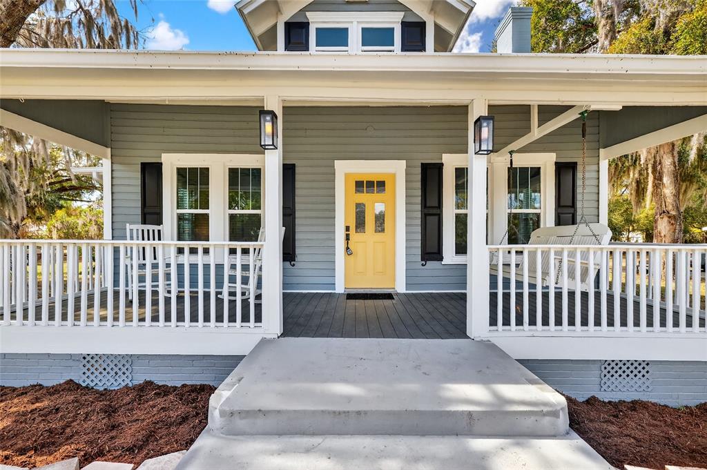 A gray house features a yellow front door, a covered porch, and a concrete walkway — 92 S TROWELL AVENUE, UMATILLA, FL
