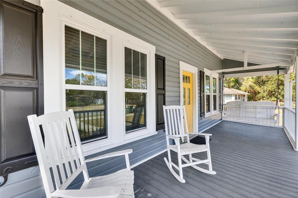 A gray-sided porch features two white rocking chairs, a hanging swing, and a yellow door — 92 S TROWELL AVENUE, UMATILLA, FL