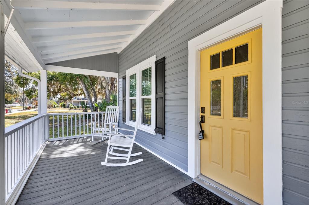 A covered porch features gray siding, a yellow front door, and two white rocking chairs — 92 S TROWELL AVENUE, UMATILLA, FL