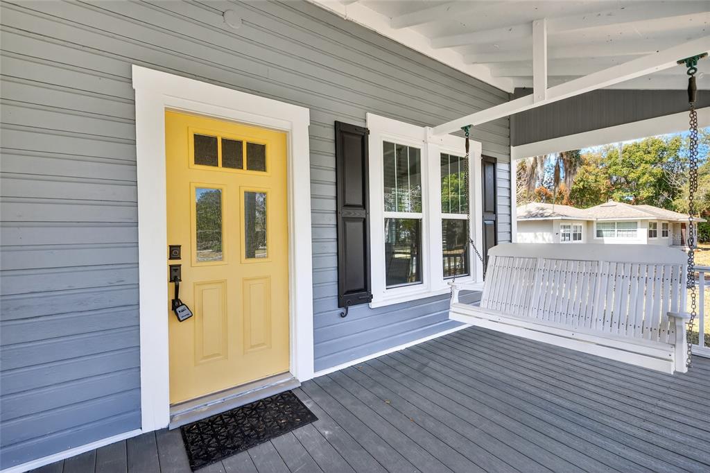 A front porch with gray siding, a yellow door, and a white hanging bench — 92 S TROWELL AVENUE, UMATILLA, FL