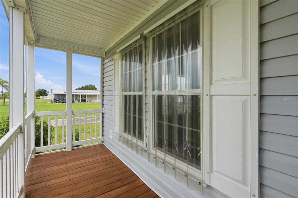 A covered porch with wood flooring, white railings, and clear plastic storm shutters on windows — 29228 MARYLU AVENUE, PUNTA GORDA, FL
