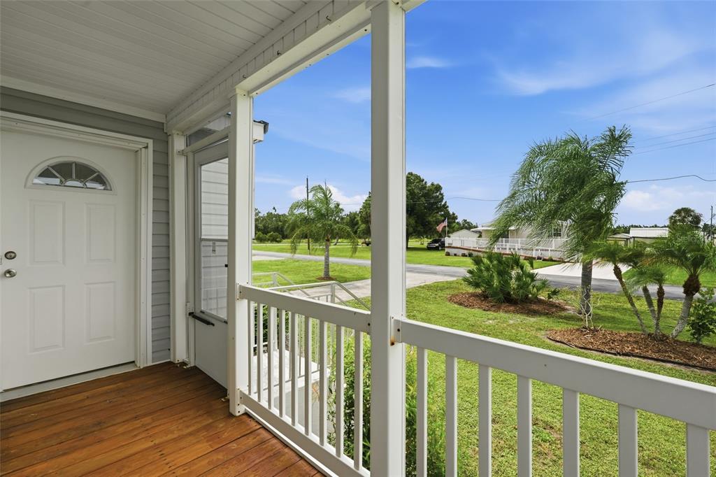 A covered wooden porch with white railings overlooks a grassy yard with palm trees — 29228 MARYLU AVENUE, PUNTA GORDA, FL