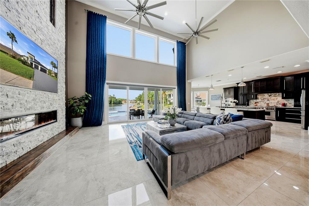 A spacious living room with a stone fireplace, large windows, and an open kitchen — 10711 CORY LAKE DRIVE, TAMPA, FL