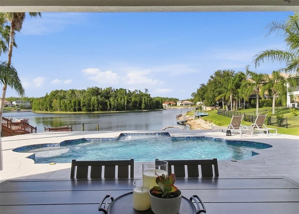A patio with a dining table overlooks a swimming pool and a lake with trees — 10711 CORY LAKE DRIVE, TAMPA, FL