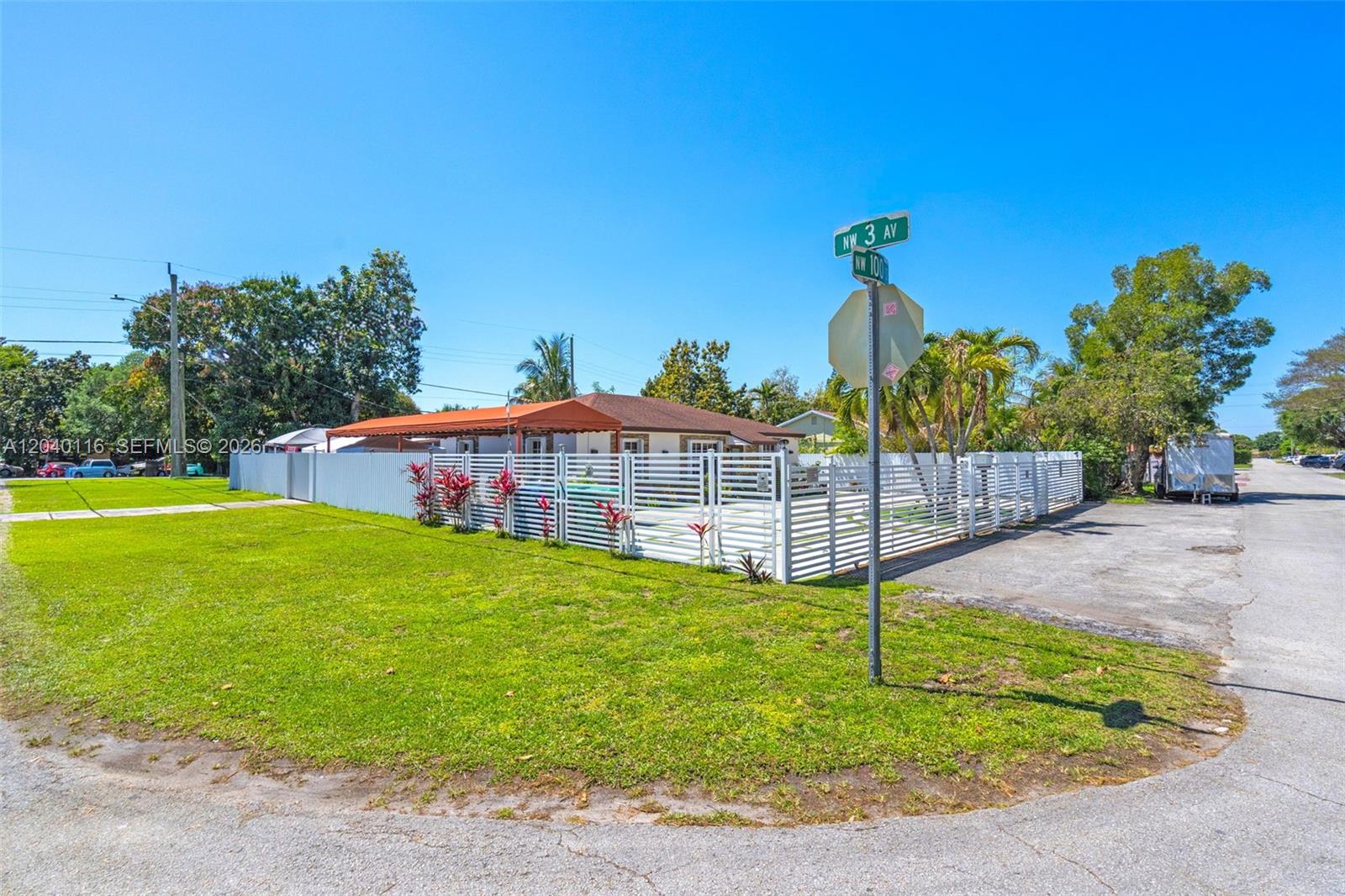 A fenced residential property with a white fence and orange awning sits on a corner lot — 302 NW 100th St, Miami FL 33150, MIAMI, FL