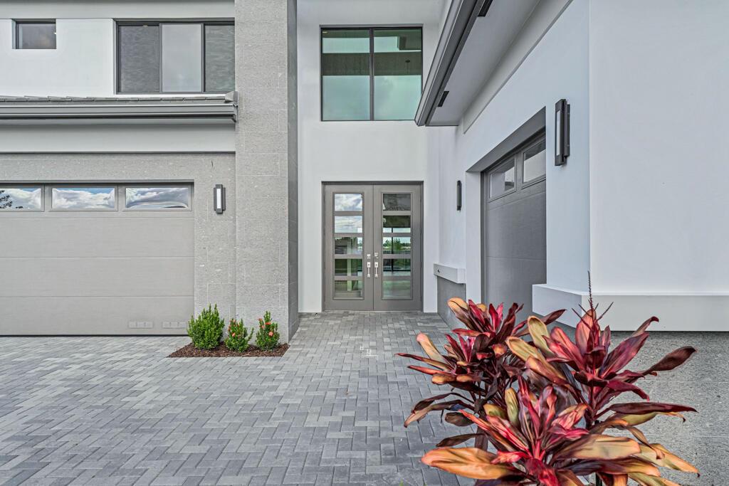 A modern two-story home exterior features a gray paver driveway, double front doors, and garages — 13531 Nesting Pines Way, Palm Beach Gardens FL 33412, PALM BEACH GARDENS, FL