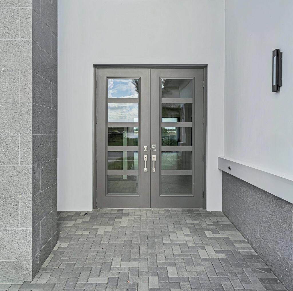 A modern double front door with glass panels sits on a gray paver entryway — 13531 Nesting Pines Way, Palm Beach Gardens FL 33412, PALM BEACH GARDENS, FL