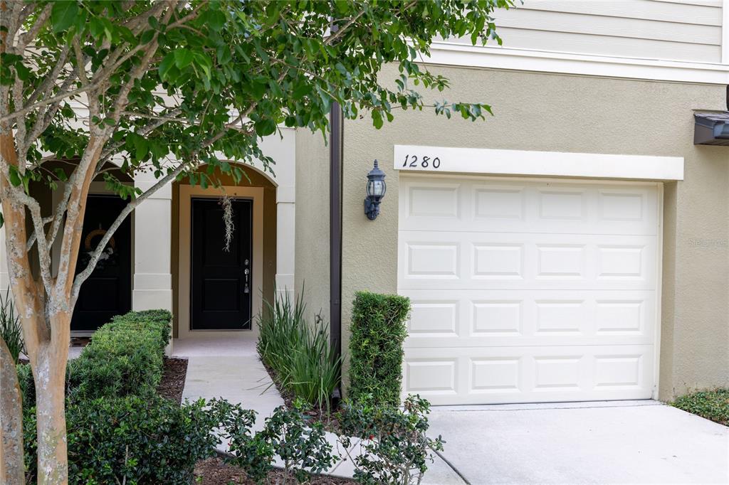 The exterior of a townhouse features a single-car garage, a front entrance, and landscaping — 1280 PAVIA DRIVE, APOPKA, FL