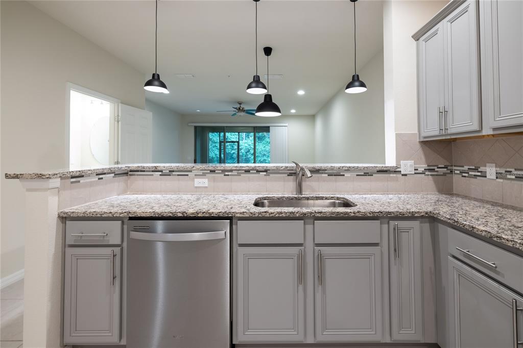 A kitchen features gray cabinets, granite countertops, a stainless steel dishwasher, and three pendant lights — 1280 PAVIA DRIVE, APOPKA, FL