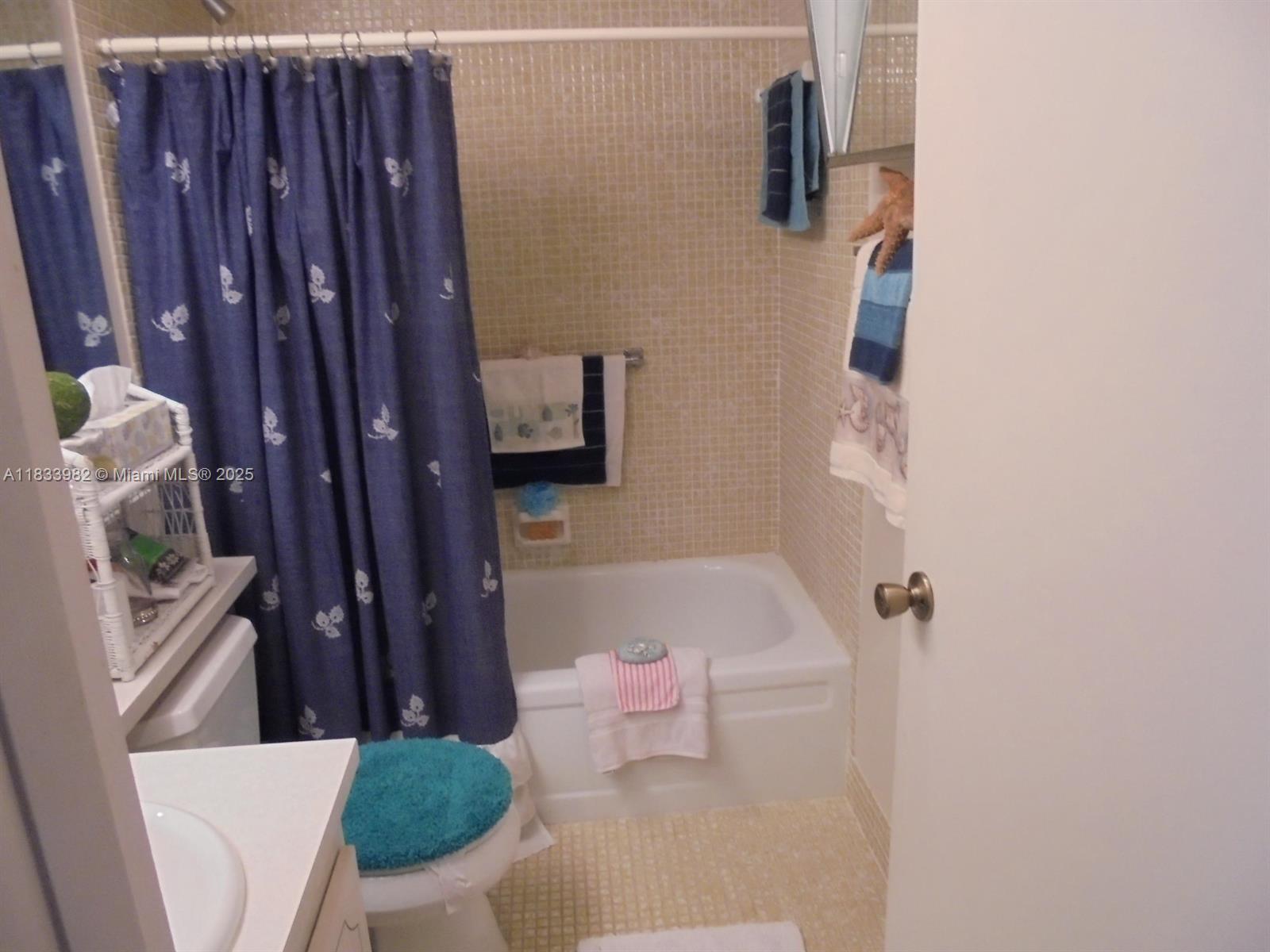 A bathroom features a white tub, a blue patterned shower curtain, and beige tiled walls — 31 Fanshaw A # 31A, Boca Raton FL 33434, BOCA RATON, FL