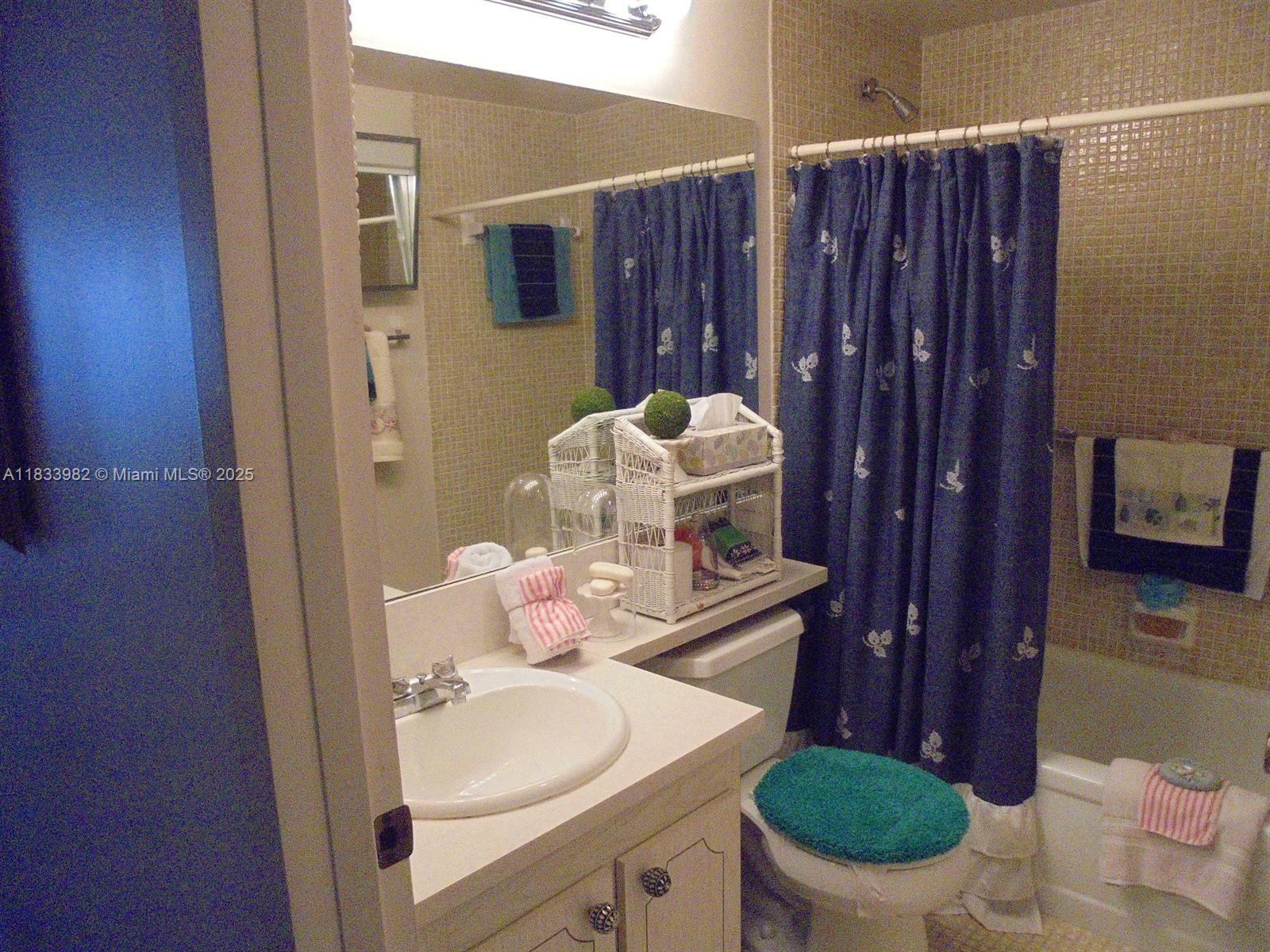 A bathroom features a vanity with a white sink, a toilet, and a blue shower curtain — 31 Fanshaw A # 31A, Boca Raton FL 33434, BOCA RATON, FL