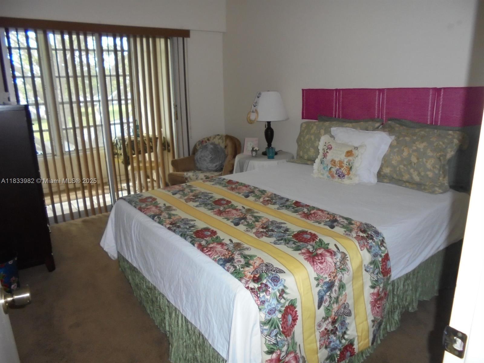 A bedroom features a floral bed runner, a pink headboard, and a sliding glass door — 31 Fanshaw A # 31A, Boca Raton FL 33434, BOCA RATON, FL