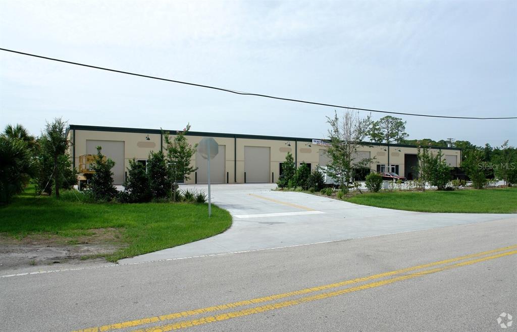 A single-story commercial warehouse building with multiple roll-up doors sits behind a paved driveway — 1220 BISCAYNE BOULEVARD, DELAND, FL