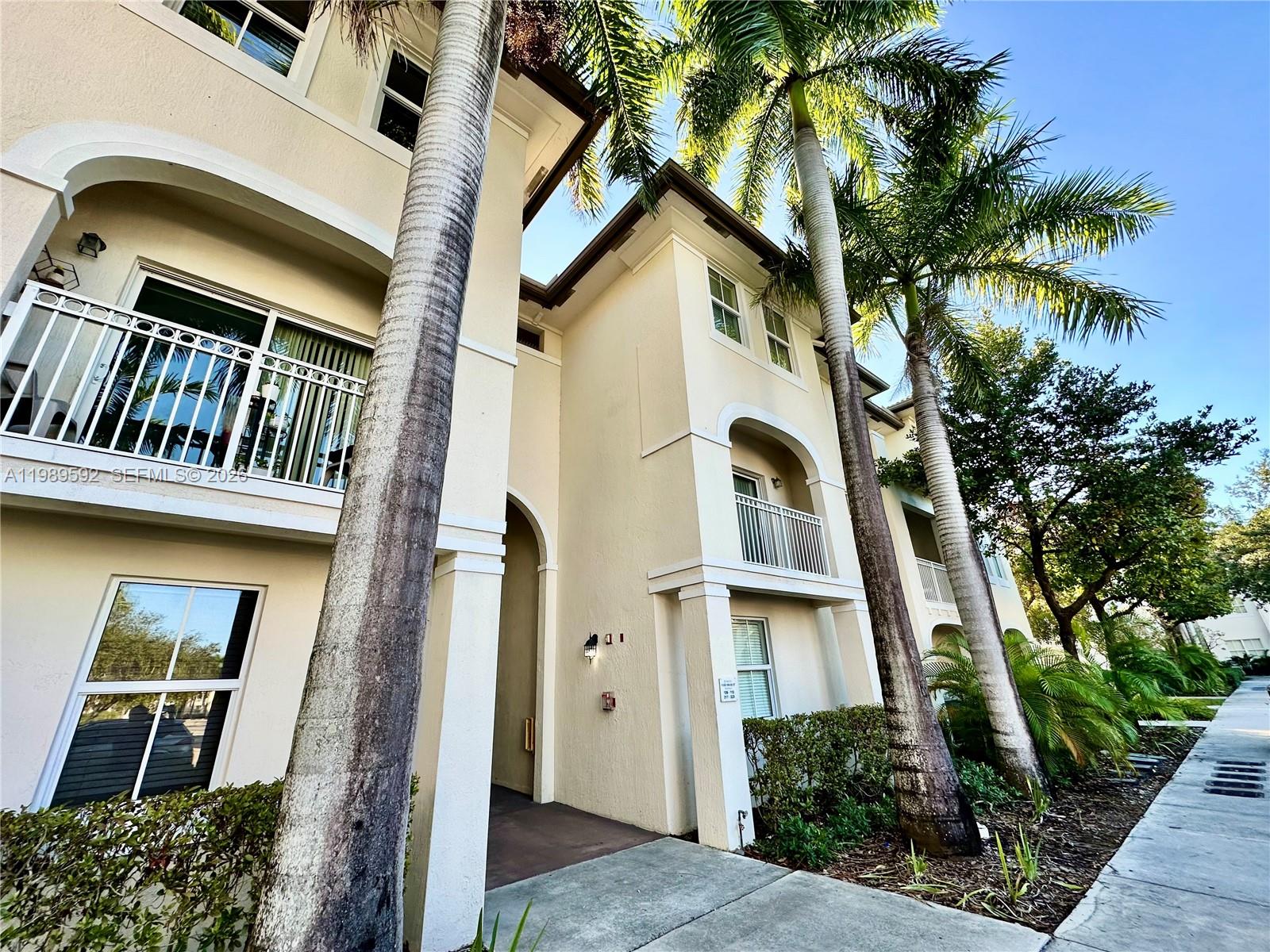 A low-angle exterior view of a multi-story stucco apartment building with palm trees — 11403 NW 89th St # 219, Doral FL 33178, DORAL, FL
