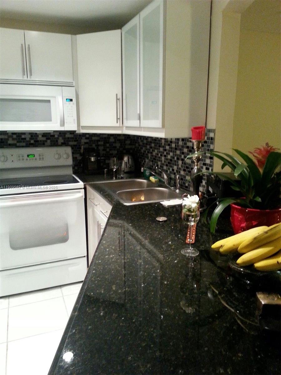 A kitchen features white cabinets, black granite countertops, a white stove, and a mosaic backsplash — 1770 NE 191st St # 1, Miami FL 33179, MIAMI, FL