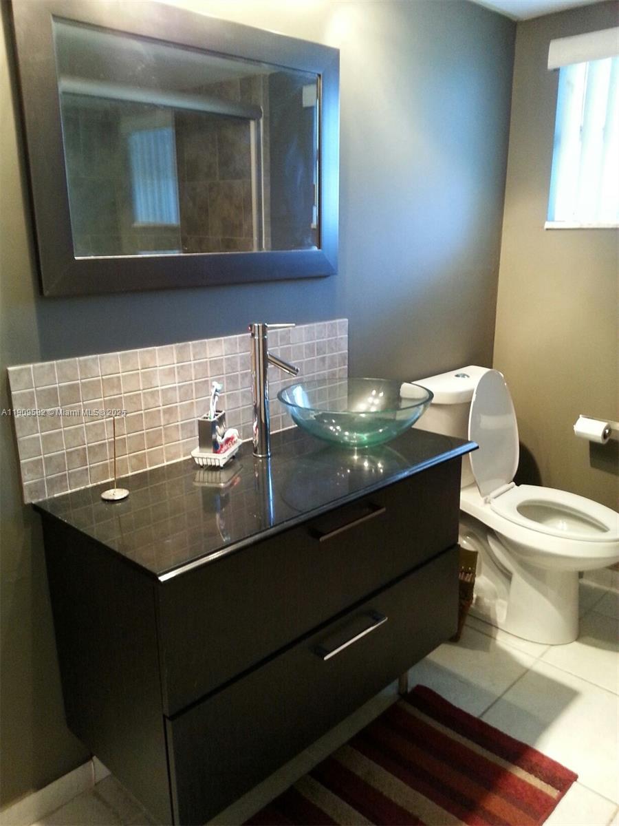 A bathroom features a dark vanity with a glass vessel sink and a wall mirror — 1770 NE 191st St # 1, Miami FL 33179, MIAMI, FL