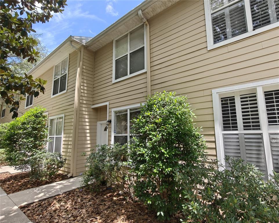 A two-story tan vinyl-sided townhouse exterior with white-trimmed windows and surrounding landscaping — 3521 SW 30TH WAY UNIT 104, GAINESVILLE, FL