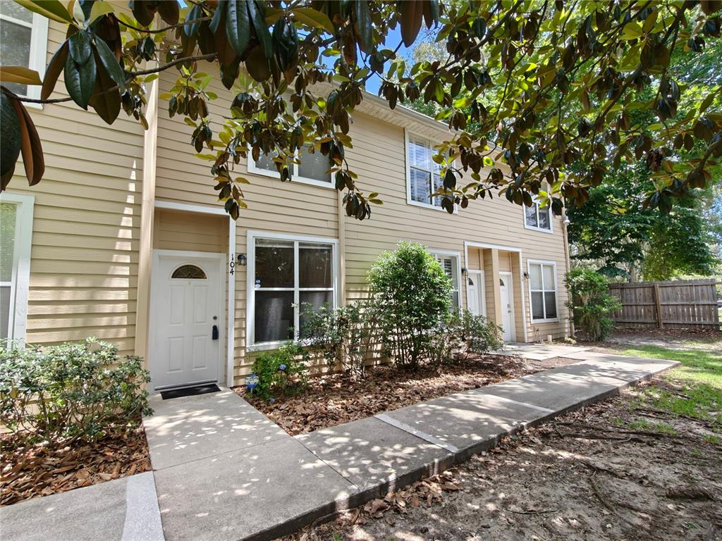 A two-story tan townhouse with a concrete walkway and a small front garden — 3521 SW 30TH WAY UNIT 104, GAINESVILLE, FL