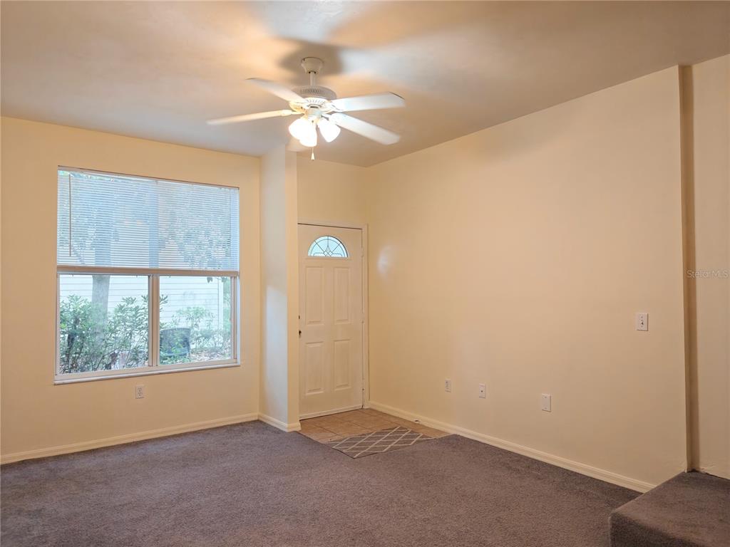 A living room features beige walls, gray carpeting, a ceiling fan, and an entry door — 3521 SW 30TH WAY UNIT 104, GAINESVILLE, FL