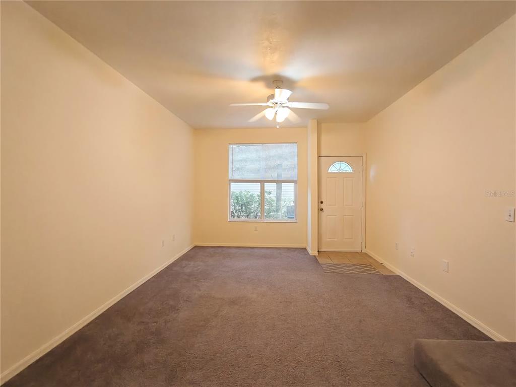 A living room with beige walls, gray carpeting, a ceiling fan, and a front door — 3521 SW 30TH WAY UNIT 104, GAINESVILLE, FL