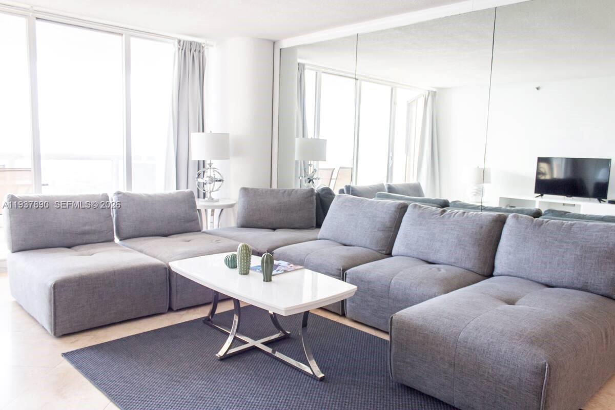 A living room features a large gray sectional sofa, a white coffee table, and mirrored walls — 1717 N Bayshore Dr # 4141, Miami FL 33132, MIAMI, FL
