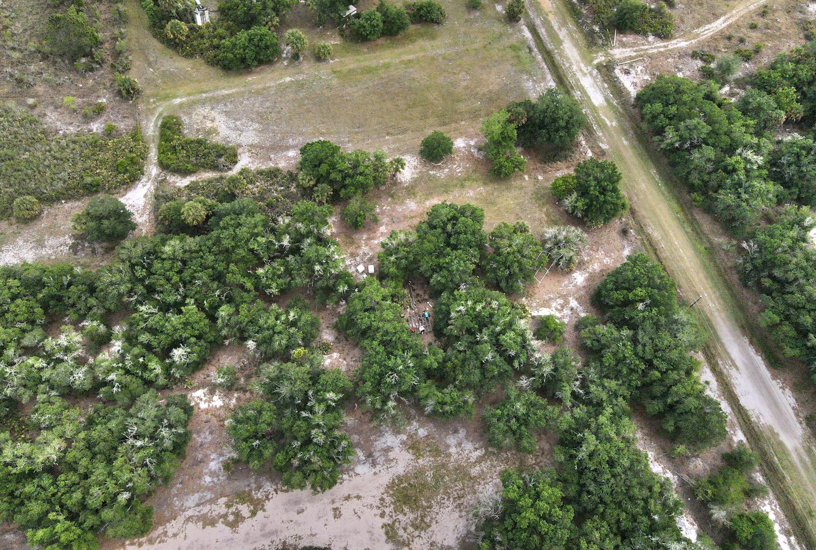 An aerial view shows a wooded lot with a dirt road and a small structure — 21877 NW 286th Street, Okeechobee FL 34972, OKEECHOBEE, FL