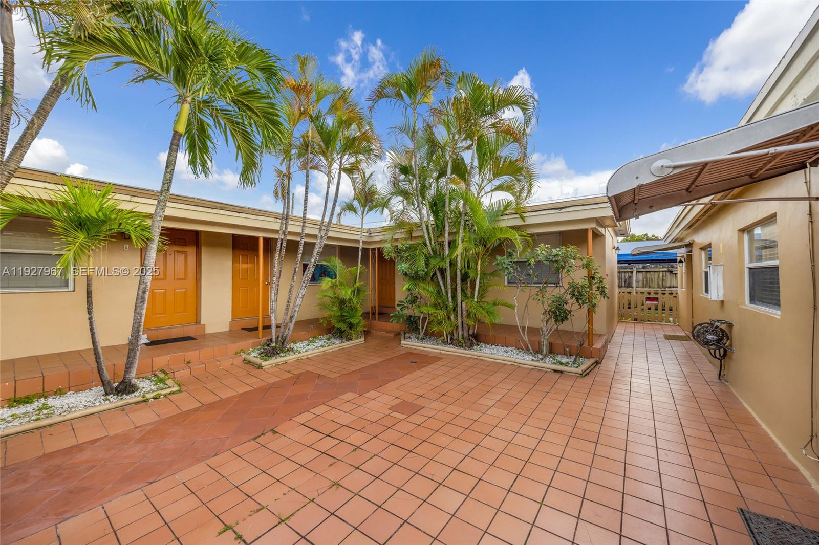 An outdoor courtyard features terracotta tile flooring, palm trees, and tan building exteriors — 6124 Pembroke Rd, Miramar FL 33023, MIRAMAR, FL
