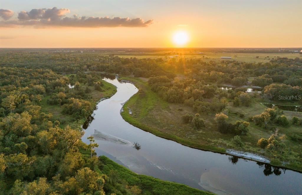 An aerial view shows a winding river flowing through a wooded landscape at sunset — 1061 HARRIS ROAD, ARCADIA, FL