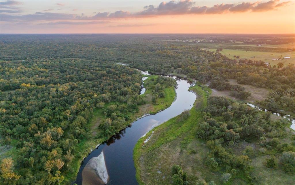 An aerial view shows a winding river flowing through a dense forest and open fields — 1061 HARRIS ROAD, ARCADIA, FL