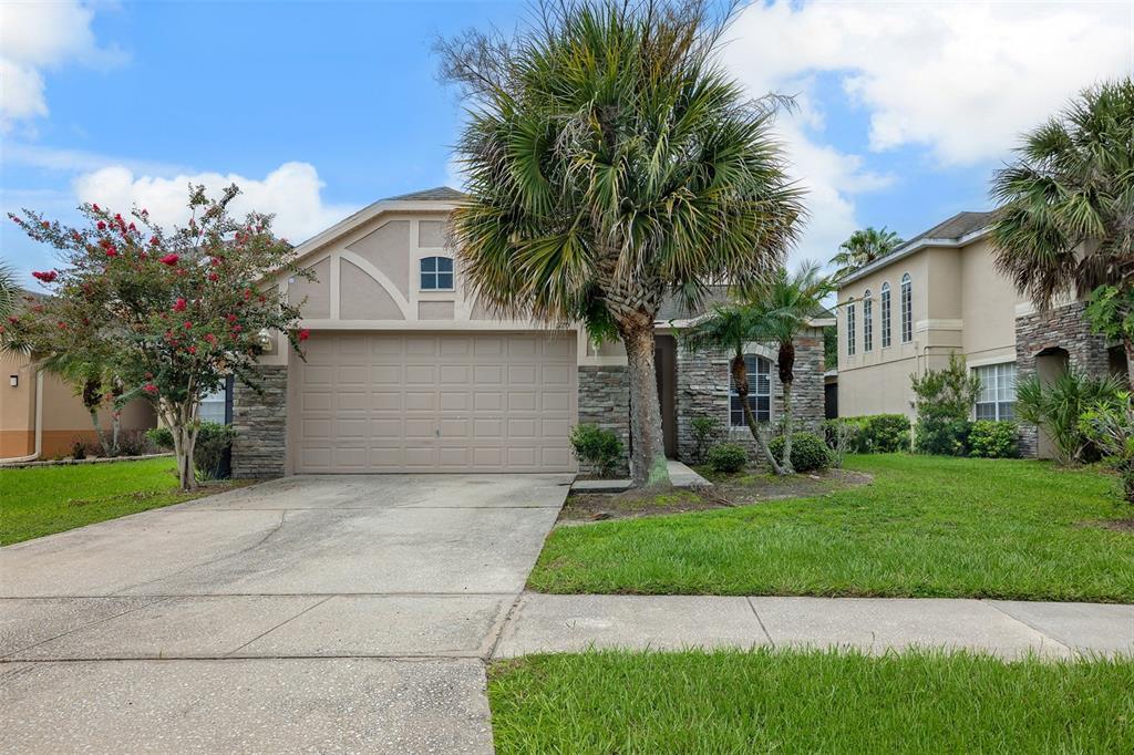 A single-story house with a beige garage, stone accents, and a large palm tree out front — 1720 BEAR BAY COVE, ORLANDO, FL