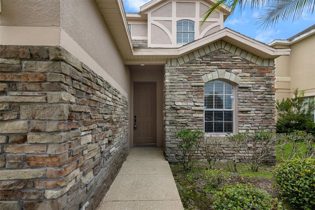 The exterior of a house features a stone facade, a brown door, and a walkway — 1720 BEAR BAY COVE, ORLANDO, FL