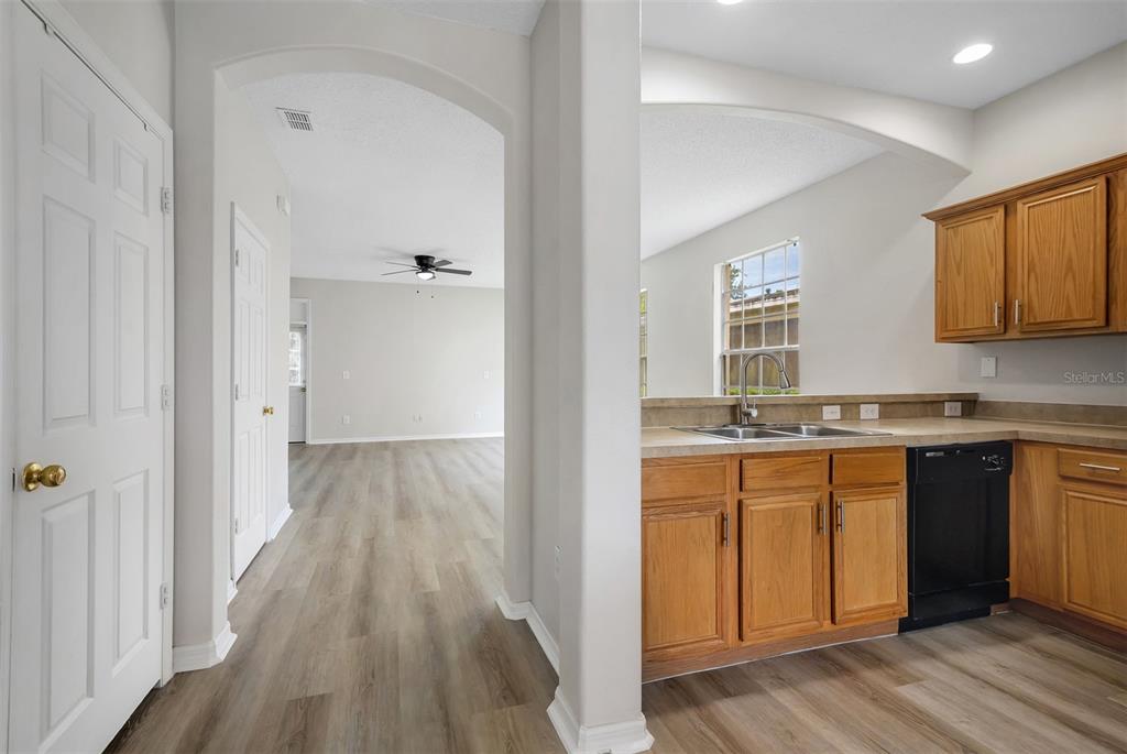 A kitchen with wood cabinets and a black dishwasher opens into a living area — 1720 BEAR BAY COVE, ORLANDO, FL