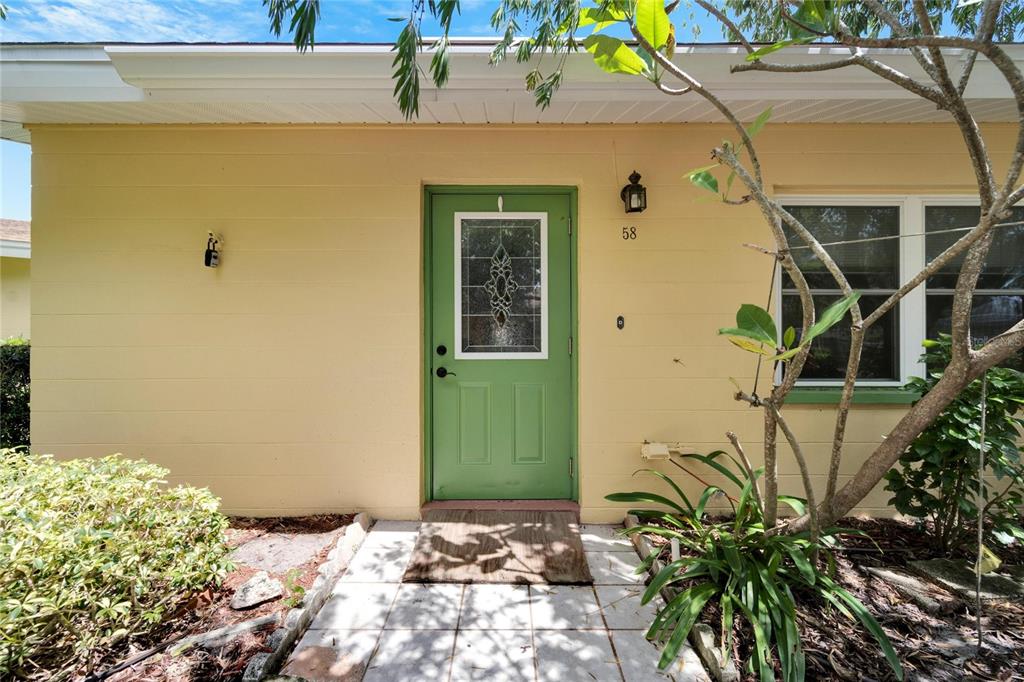 The exterior of a house features a light yellow wall, a green front door, and a walkway — 401 DORCHESTER PLACE UNIT 58, SUN CITY CENTER, FL
