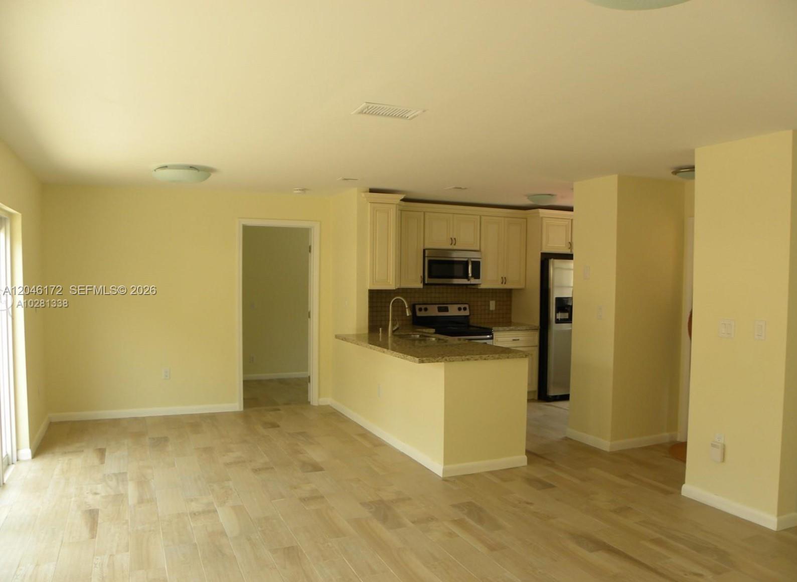 An open-concept kitchen with light-colored cabinets and granite countertops overlooks a living area — 14742 SW 92nd St Rd, Miami FL 33196, MIAMI, FL