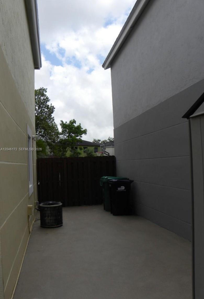 A narrow concrete side yard sits between two residential buildings with trash bins and fencing — 14742 SW 92nd St Rd, Miami FL 33196, MIAMI, FL