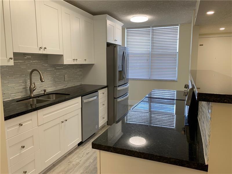 A kitchen features white cabinets, black countertops, a stainless steel refrigerator, and a breakfast bar — 250 Jacaranda Drive # 203, Plantation FL 33324, PLANTATION, FL