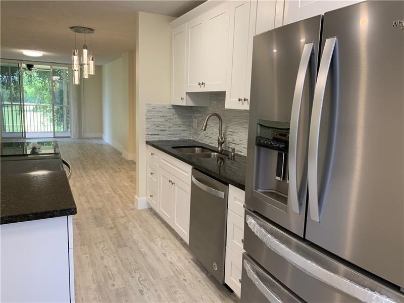 A kitchen features white cabinets, dark countertops, stainless steel appliances, and light wood-look flooring — 250 Jacaranda Drive # 203, Plantation FL 33324, PLANTATION, FL