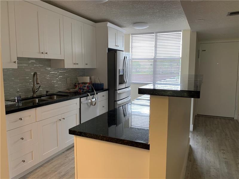 A kitchen features white cabinets, black countertops, a stainless steel refrigerator, and a breakfast bar — 250 Jacaranda Drive # 203, Plantation FL 33324, PLANTATION, FL